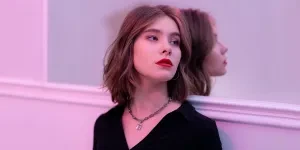 Stylish woman with red lips and necklace reflecting in mirror indoors