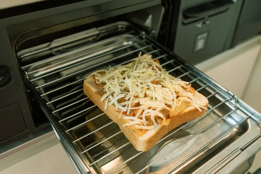 The image displays an electric micro-oven containing bread, likely mid-toast, with a warm glow emanating from within.