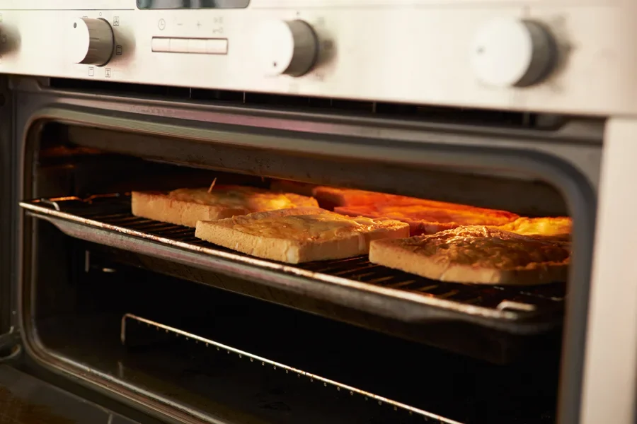 The image displays an electric micro-oven containing bread, likely mid-toast, with a warm glow emanating from within.