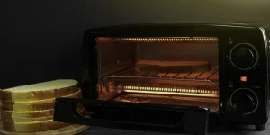 Gambar tersebut memperlihatkan oven mikro listrik berisi roti, kemungkinan sedang dipanggang, dengan cahaya hangat yang terpancar dari dalamnya.