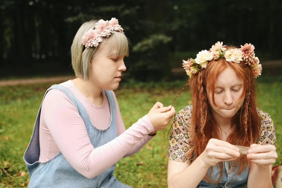 Two women enjoying a serene outdoor setting, braiding hair with flower crowns