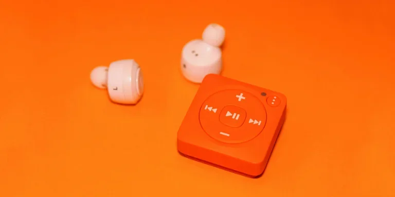 Белые наушники рядом с оранжевым музыкальным плеером