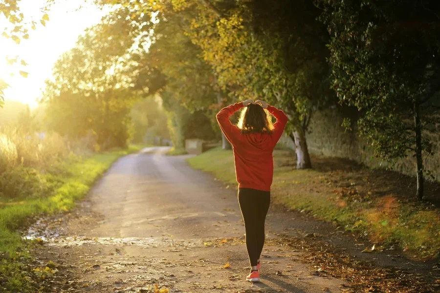 Женщина идет по тропинке рядом с деревьями и полем.