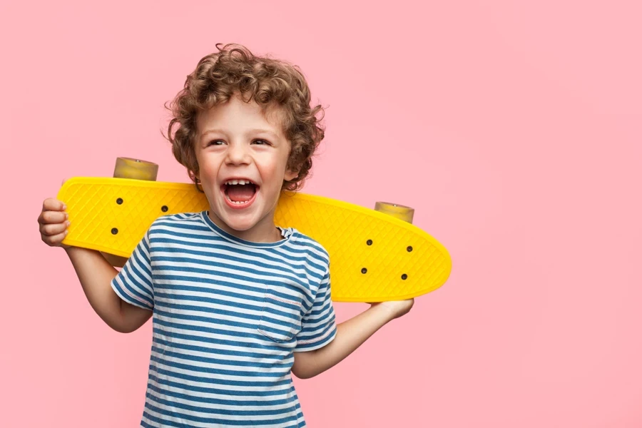 Young boy with curly hair holding yellow skateboard