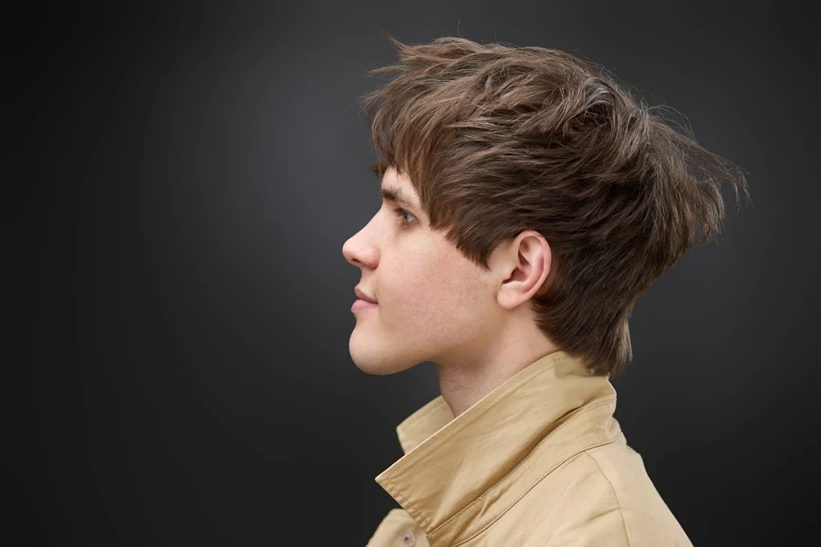 Young man with brown hair styling a messy mod cut