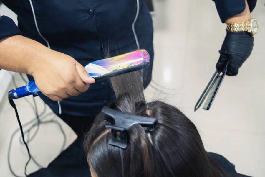 top shot of a woman straightening the hair of a brown-haired woman in a beauty salon with a hair straightener and comb