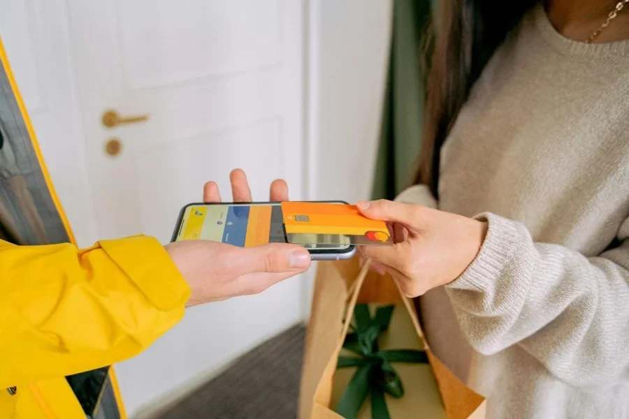 A Person in Knitted Sweater Holding a Credit Card while Putting on Top of the Phone