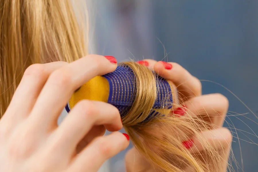 A blond woman wrapping hair around a heatless roller.