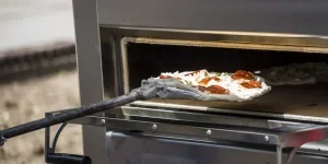 Une pizza au pepperoni entrant dans un four à pizza au propane