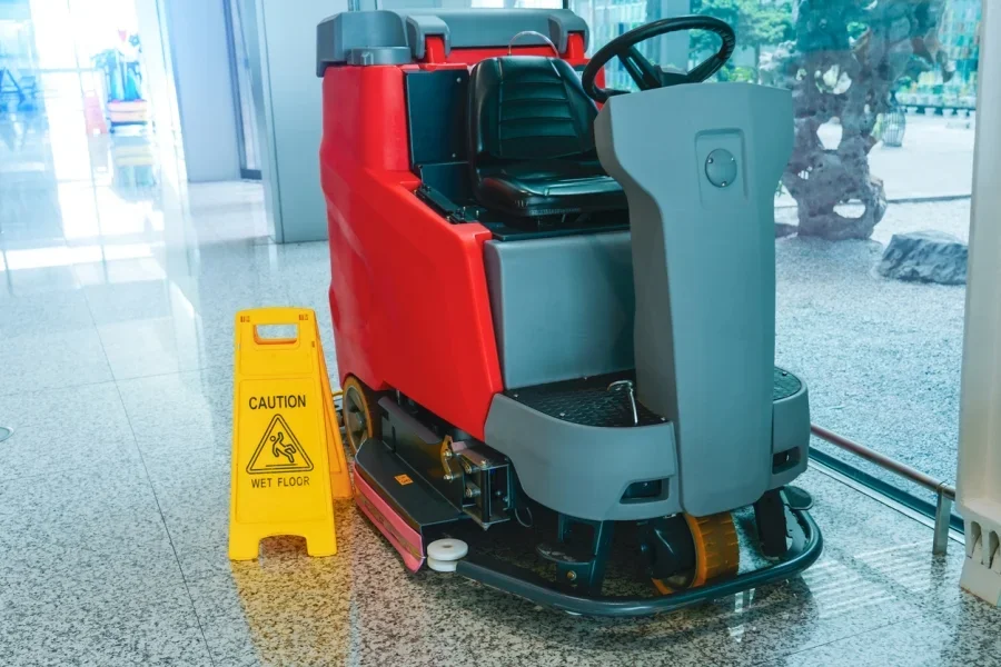 A red and black floor scrubber machine on a wet floor