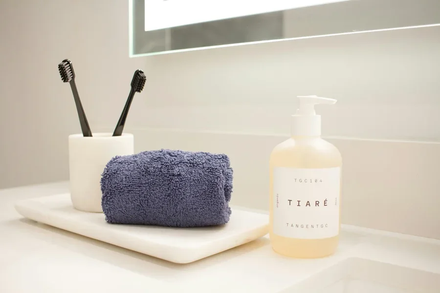 A sleek bathroom countertop adorned with a fluffy towel, a chic handwash, and a white toothbrush holder. The clean and organized setup adds a touch of elegance to the space