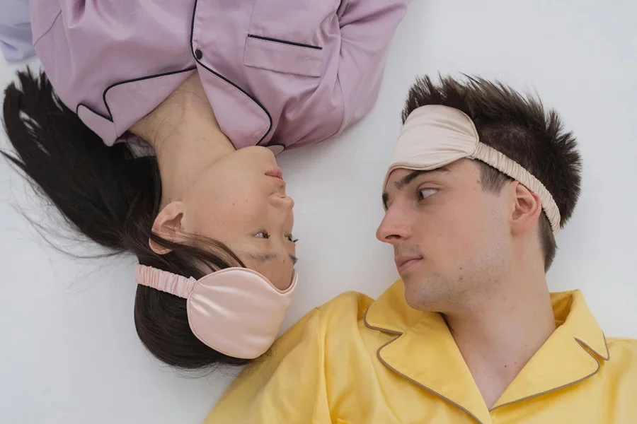 Asian woman and Caucasian man lying face to face in colorful pajamas and sleep masks