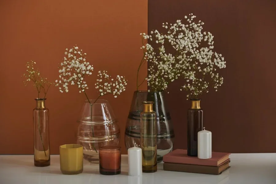 Beautiful aromatic still life composition with flowers in glass container and scented candle on brown background