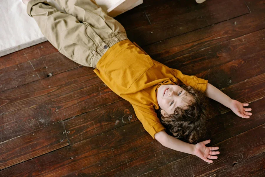 Junge im gelben T-Shirt liegt auf braunem Holzboden
