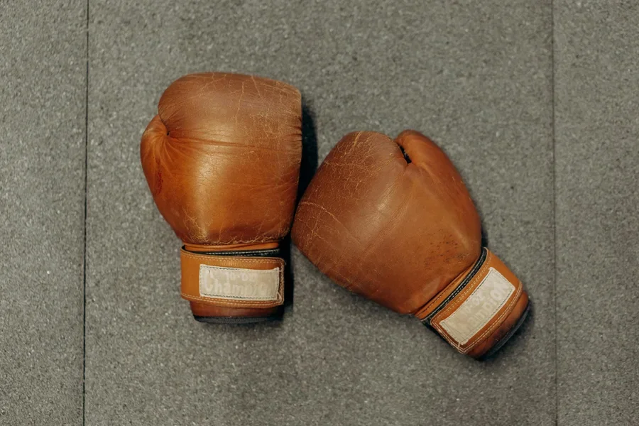 Guantes de boxeo de cuero marrón sobre una superficie de gimnasio gris texturizada