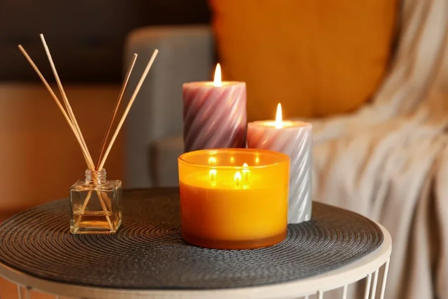 Burning candles and reed air freshener on table indoors