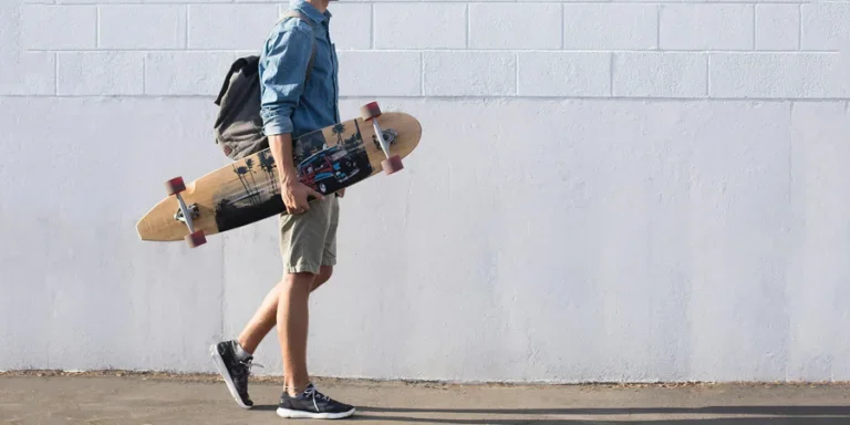Casual young man walking with longboard against a white brick wall in Sanger, California