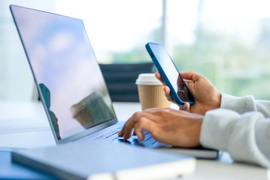 Close up of a Businessman working on a laptop computer and holding and looking at a mobile phone in the office