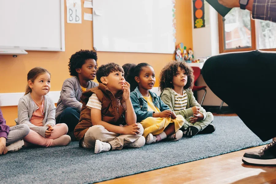 Estudiantes de primaria se sientan y escuchan una historia de su maestra