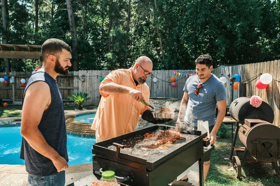 Men next to pool cooking burgers on outdoor griddle