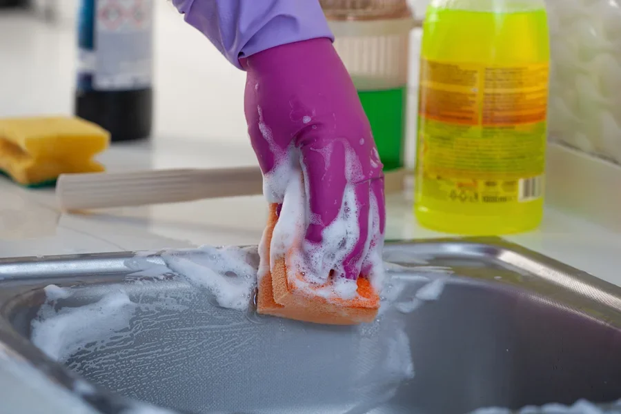 Person cleaning a kitchen sink with a sponge and cleaner