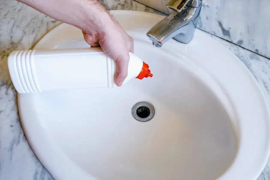 Person pouring in a sink cleaner from a white bottle
