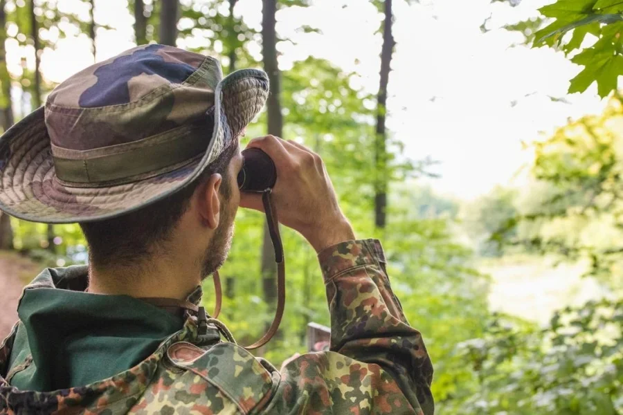 Soldado con uniforme de camuflaje observando con binoculares en el bosque