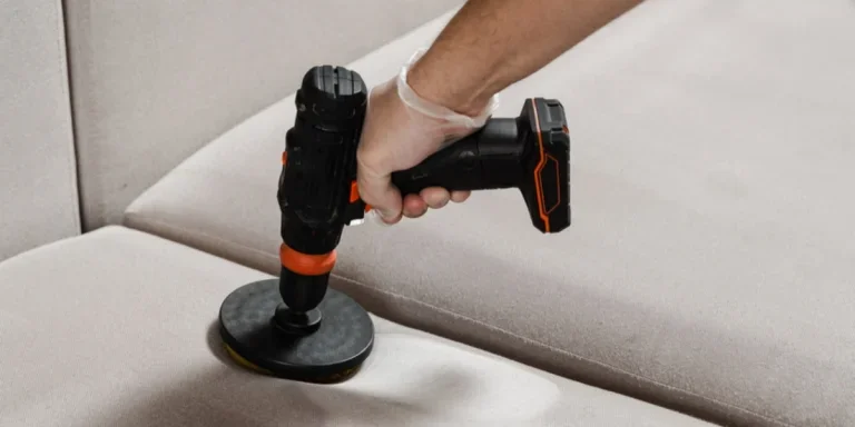 Someone using a drill with a brush to clean a couch