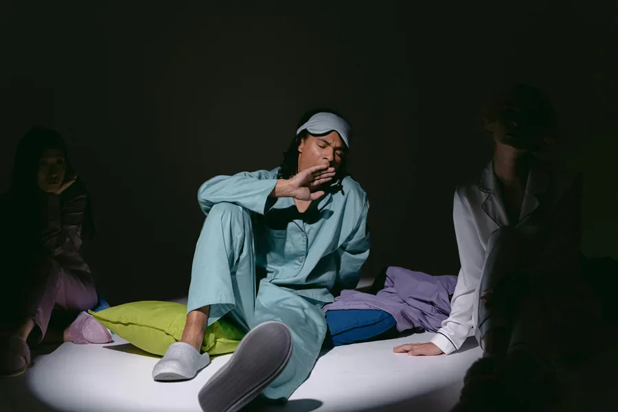 Three adults in pajamas relaxing in dim light, wearing sleep masks