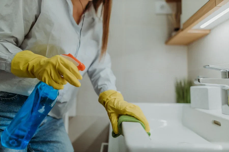 Woman holding a bottle of sink cleaner with yellow gloves