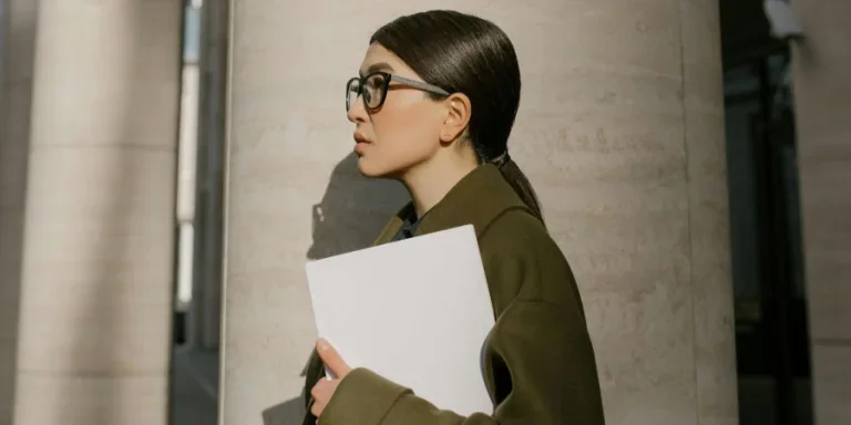 Mujer con abrigo verde de pie junto a una columna de hormigón