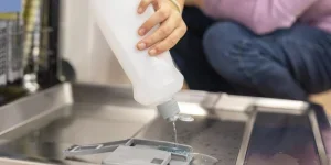 Женщина наливает ополаскиватель в отделение посудомоечной машины.