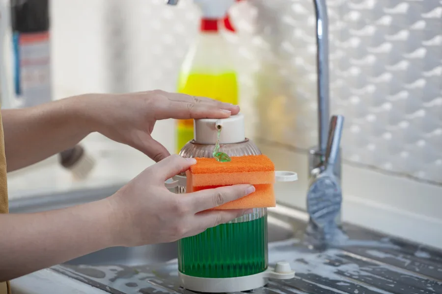 Une femme appuie sur la pompe pour faire couler du nettoyant liquide sur une éponge.