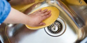 Woman using large sponge to buffer stainless steel sink