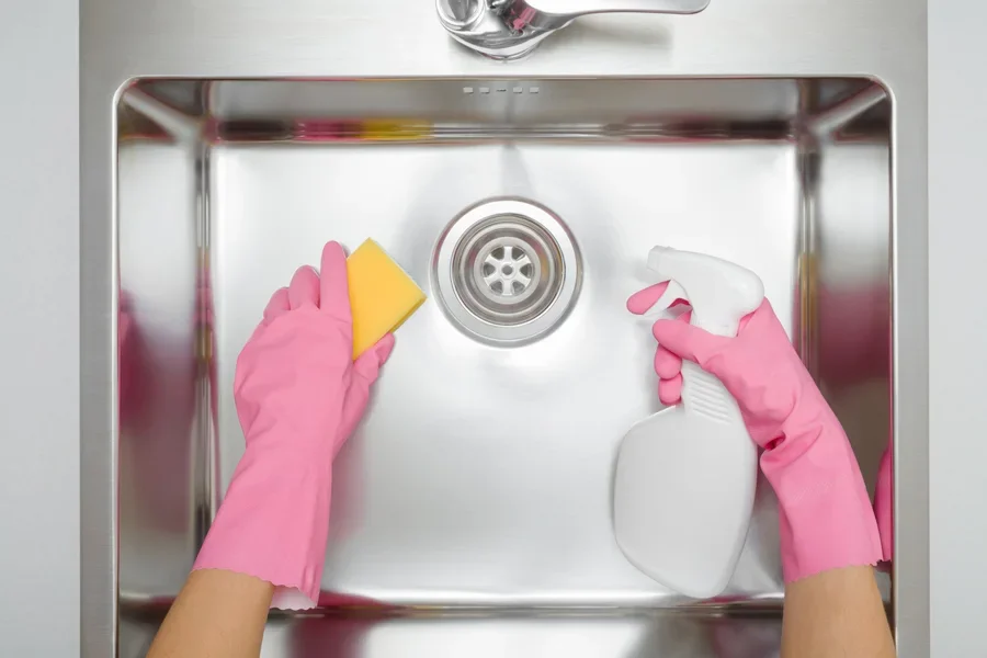 Femme portant des gants roses utilisant un spray dans l'évier de la cuisine