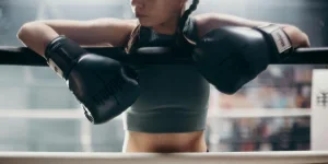 Young female boxer resting on the ropes in a boxing gym, emphasizing strength and focus
