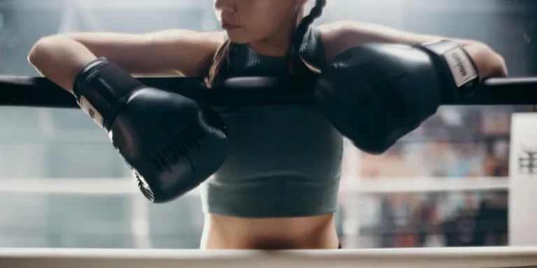 Junge Boxerin ruht sich in einem Boxstudio auf den Seilen aus und betont Kraft und Konzentration