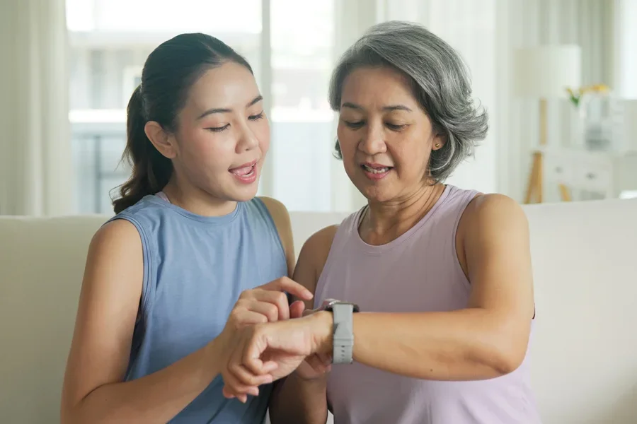 Una persona más joven le muestra a una persona mayor cómo usar un reloj inteligente.