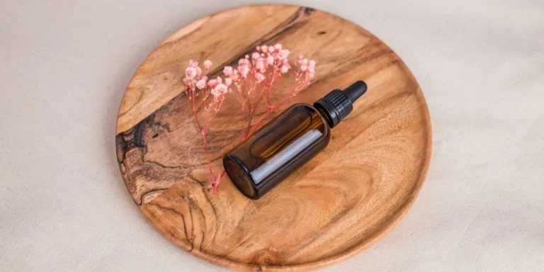 Una botella marrón de suero en una bandeja de madera con flores rosas.