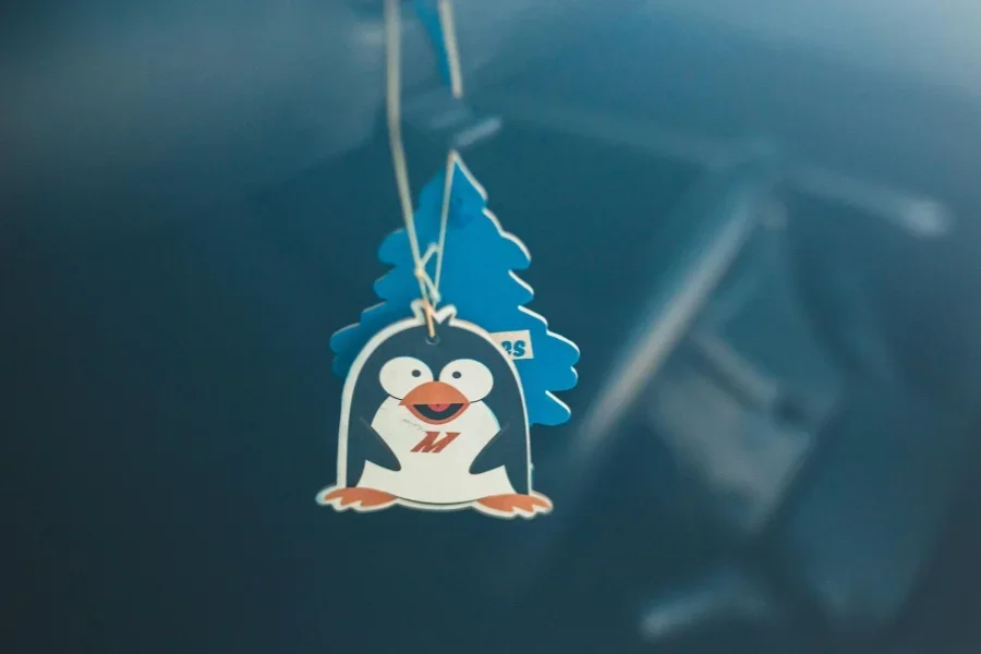 Милый освежитель воздуха в виде пингвина, висящий в машине на мягком фокусном фоне.