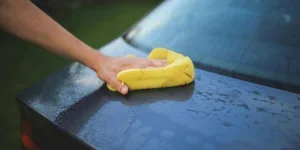 A hand with a yellow sponge cleaning a car