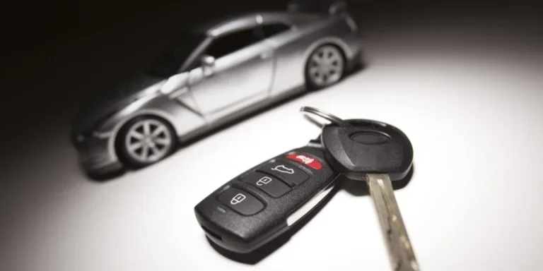 Ключ от машины, пульт дистанционного управления и размытый автомобиль на заднем плане