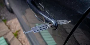Close-up of a locksmith tool inserted into a car door lock, demonstrating security access