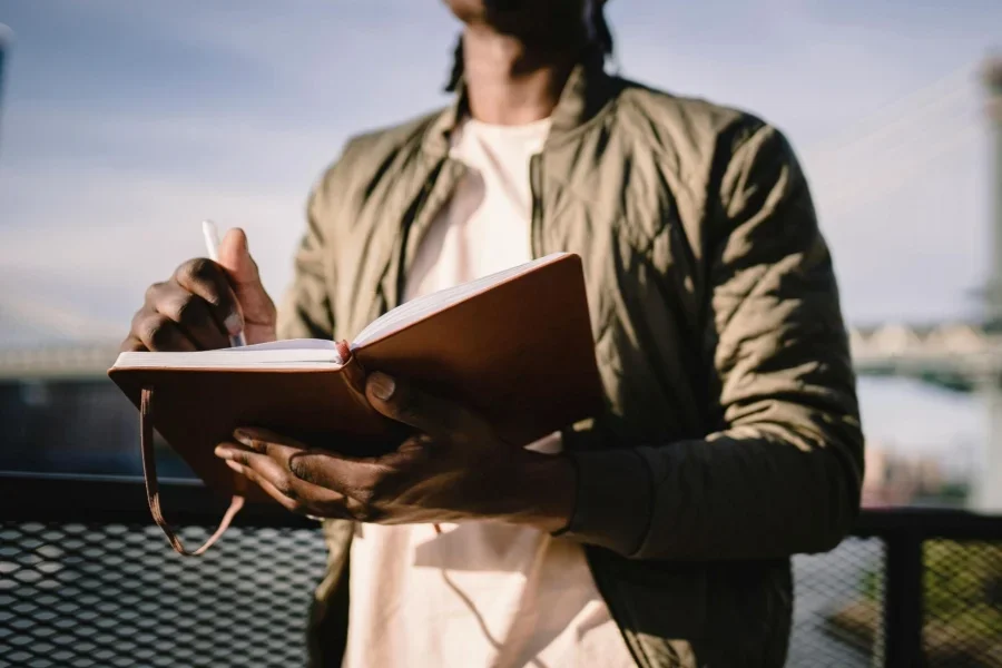 Potong gambar pria kulit hitam yang tidak dikenali sedang menulis di buku catatan di balkon