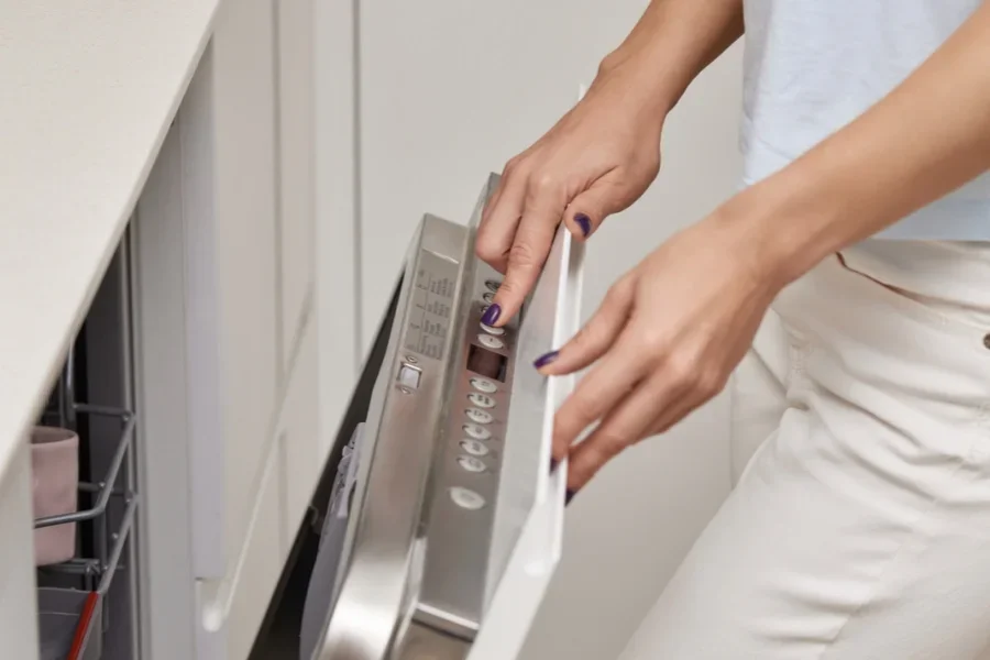 Female Hand Turning on Dishwasher Machine in Kitchen
