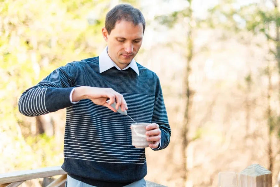 Glas Wasser und Teetassen draußen auf dem Hinterhofdeck und dem Holzzaun im Frühling oder Herbst auf einem Mann mit Matcha-Schneebesen