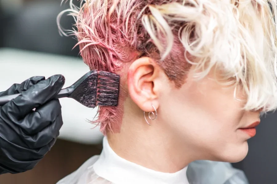 La mano del peluquero con guantes negros pinta el cabello de la mujer de color rosa.