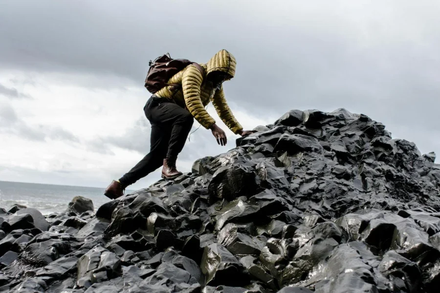 Pria Berkerudung dan Celana Hitam Memanjat Tumpukan Batu