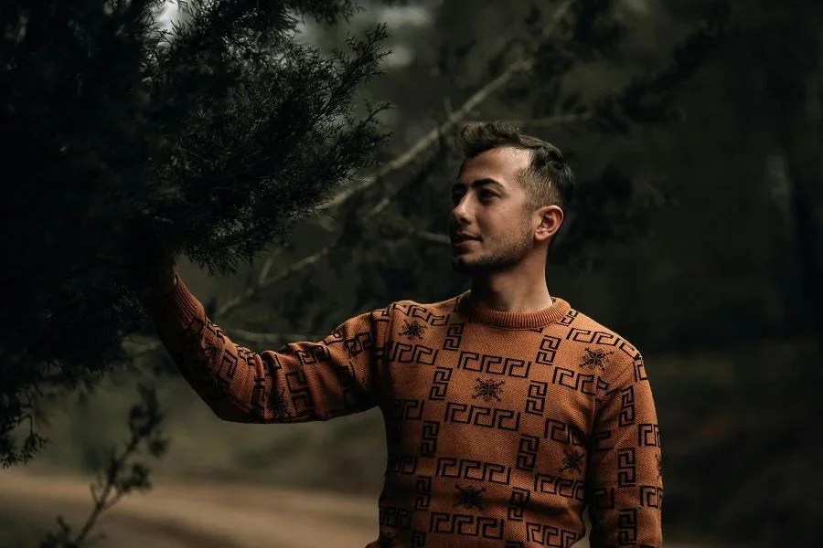 Homem de suéter laranja segurando um galho de árvore