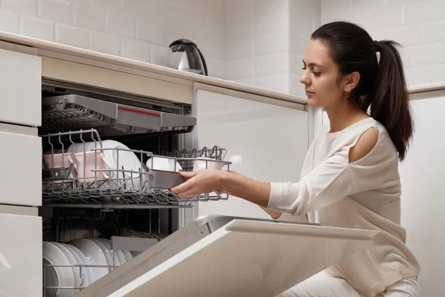 Pretty Woman Unloading from Open Dishwasher Machine with Clean Utensils Inside
